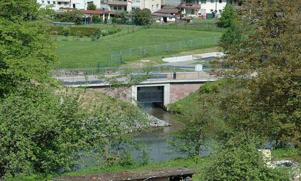 Foto des Absperrbauwerks am Auslauf vom gegenüberliegenden Berghang